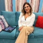 Vivianne Verschae sentada en un sofá azul durante una entrevista televisiva, con expresión cálida y profesional.