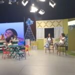 Vivianne Verschae participando en un programa de televisión, sentada junto a otra invitada en un set decorado con temática navideña.
